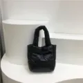 Close-up view of the black quilted puffer tote bag, showing soft padded nylon texture and details. - Black