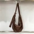 Detailed shot of brown soft leather hobo bag hanging, showing pleated design and strap knot. - Brown