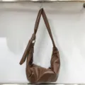 Close-up detail of the soft pleated leather texture and unique shoulder strap knot design. - A Brown