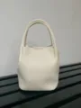 Detailed view of a mini cream leather bucket tote handbag, showing texture and handle design. - White
