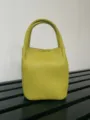 Detailed shot of a chartreuse leather bucket handbag featuring dual top handles and clean stitching. - Neon Yellow