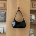 Detail shot of a black soft leather shoulder bag with braided strap and heart pouch on wood. - Black