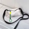 Detail view of casual white crossbody bag with wide black strap and green charm, close up. - Off White