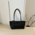 Λεπτομερής λήψη μαύρης πλεγμένης δερμάτινης τσάντας ώμου με κομψό διάτρητο σχέδιο. - Μαύρο