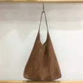 Close-up detail shot of the brown suede slouchy hobo shoulder bag hanging on a wooden rod. - Suede Brown