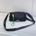 Detail view of the black nylon crossbody bag featuring green and yellow decorative rope charm. - Black
