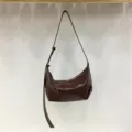 Detail view of minimalist glossy brown dumpling shoulder bag, hobo handbag strap close-up - Coffee