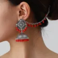 Close-up detail of Indian ethnic silver oxidized jhumka earrings with red beads hair chain. - Red