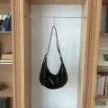 Detailed shot of a black soft leather slouchy crescent shoulder bag hanging in a chic bookshelf scene. - Black
