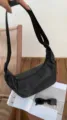 Close-up detail of a black nylon crescent crossbody bag in a casual lifestyle scene. - Black
