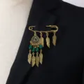 Close-up detail of retro gold safety pin brooch with feather charms and green bead drops. - Green