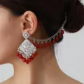 Close-up detail shot of ethnic hollow-out carved silver stud earrings with red bead tassels. - Silver Red