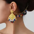 Close-up detail of ethnic hollow-carved gold earrings with colorful beads and hair chain. - Gold Colorful
