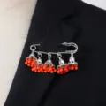 Close-up detail of bohemian vintage bell tassel brooch featuring bright orange beads on black suit. - Orange Red
