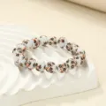 Close-up shot of white ceramic bead bracelet with delicate black and orange floral patterns. - Black