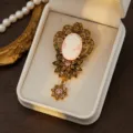 Detailed view of vintage cameo rhinestone brooch with ornate gold filigree and pendant. - Style 3