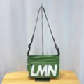 Green crossbody bag detail showing large LMN print and adjustable black shoulder strap. - New Green