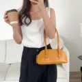 Close-up of a stylish yellow shoulder baguette bag worn on arm in a clean indoor lifestyle scene. - Yellow