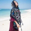 Detail view of a bohemian floral print cotton linen scarf shawl with handmade tassels on beach. - L04 / Above 175cm
