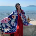 Outdoor beach scene detail showcasing a stylish blue floral printed shawl with red trim design. - Style 2318