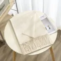 Close-up of soft beige winter cashmere-like fringed scarf detail on wooden table, cozy style. - Color 19