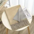 Detailed close-up of a cozy two-tone cashmere-feel winter scarf with delicate fringes on table. - Color 27