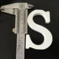 Close-up detail shot of a white wooden letter S being measured with a metal caliper tool. - White Letter S