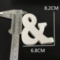 White wooden ampersand symbol detail shot showing precise dimensions with metal caliper. - White &