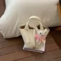 Elegant cream leather bucket bag with lock charm and cute knitted rabbit pendant. - With Pendant / White