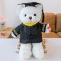 Detalle del adorable osito de peluche graduado con birrete, toga negra y diploma. - 30cm / Oso blanco con cuello amarillo y borlas negras