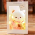 Close-up of a cute plush lamb doll in a white window gift box decorated with warm fairy lights. - Pink Hoodie Lamb [Gift Bag + Light Strip] / 22cm