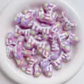 Close-up detail of iridescent acrylic macaron bow beads with white drip and green star decor. - Purple + White