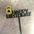 Close-up detailopname van de zwarte acryl Happy Birthday taarttopper met gele robot figuur. - Gouden robot Happy Birthday