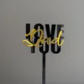 Detailed close-up of black and gold acrylic Love You Dad cake topper for Father's Day party. - LOVE YOU Dad Artistic Font Pick / Width Approx 8CM / Black & Gold