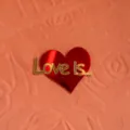 Roter Acryl Herz Tortenaufsatz mit goldener Love is Text Detailaufnahme zum Valentinstag. - Love Is (Spiegelrote Basis + Goldene Oberfläche)