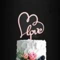 Detailed close-up shot of pink acrylic love heart cake topper displayed on a sweet dessert cake. - Heart Rose Gold Love / Approx. 10cm Width