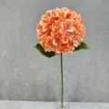 Detailed close-up of artificial peach hydrangea flower with green leaves in clear glass vase. - Orange Pink