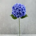 Close-up detail of artificial blue hydrangea flower with green leaves and stem in glass vase. - Dark Blue