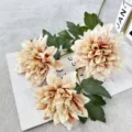 Vue détaillée de fleurs de dahlias artificielles champagne élégantes avec feuilles vertes. - Café Clair