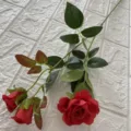 Primo piano dettagliato di un ramo di rosa rossa artificiale con foglie verdi per decorazione. - Rosso scuro