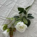 Dettaglio ramo di rosa bianca artificiale, testa in seta e foglie verdi, primo piano. - Bianco
