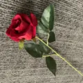 Gros plan détaillé d'une rose artificielle en velours rouge avec des feuilles et une tige. - Rouge