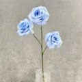 Close-up detail of three blue artificial roses with green stem in clear glass vase. - Blue
