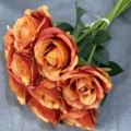 Nahaufnahme eines künstlichen orangefarbenen Rosenstraußes mit grünen Blättern und Stielen. - Sonnenuntergang
