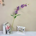 Artificial purple pansy orchid flower stem in glass vase with books and calendar decor. - Deep purple
