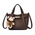 Brown leather bucket bag with metal lock clasp and cute knit bear charm accessory. - Dark Brown