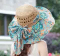 Detaillierte Nahaufnahme des breiten Sonnenhutes mit Strohkrone und bunter Paisley-Schleife. - Khaki & orangefarbener Stoff