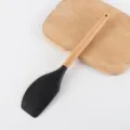 Spatola da cucina in silicone nero con manico in legno naturale e tagliere di fondo. - Spatola