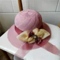 Vista dettagliata del cappello di paglia rosa con nastro e decorazione di fiori di perla. - Con Cordino Antivento / Viola chiaro