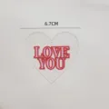 Close-up detail of acrylic heart cake topper with pink and red love you letters text. - Love Heart Style